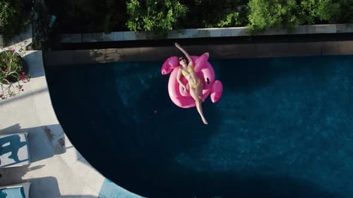 Woman Relaxes on Flamingo Float in Tropical Pool