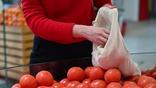 Mujer recogiendo tomates en una bolsa reutilizable en una tienda. Temáticas del Día de la Tierra y la Ecología. Cámara lenta
