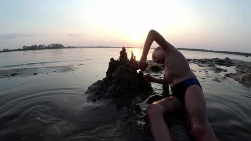 Silhouette of a Child on the Beach Building a Sand Castle at Sunset