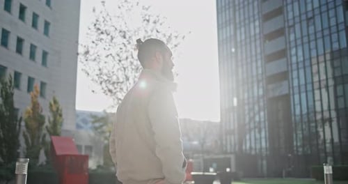 A Young Man with a Stylish Trendy Hairstyle and Beard in Casual Clothes Stands on the Street in the