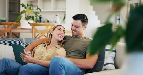 Couple Relaxing on Sofa Looking at Tablet