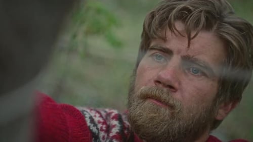 Man Tying Rope around Tree to Set Up Camping Tent in Woods