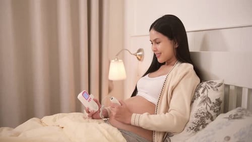 Femme enceinte tenant un doppler foetal de poche pour écouter le rythme cardiaque du bébé sur le ventre
