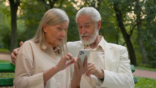 Silver Haired Couple Using Smartphone in Green Park