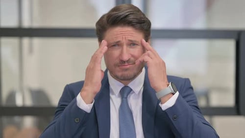 Stressed Businessman Massaging Temples in Office Setting