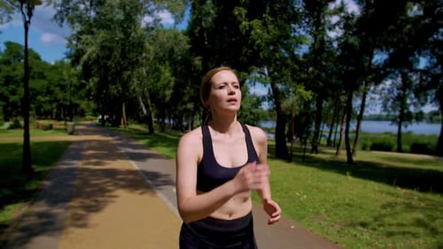 Motivated Sporty Fit Middle Aged Female Runner Jogging in Summer Park