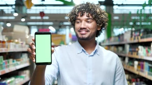 Male customer shows green screen phone smartphone standing in supermarket shopping center mall groce