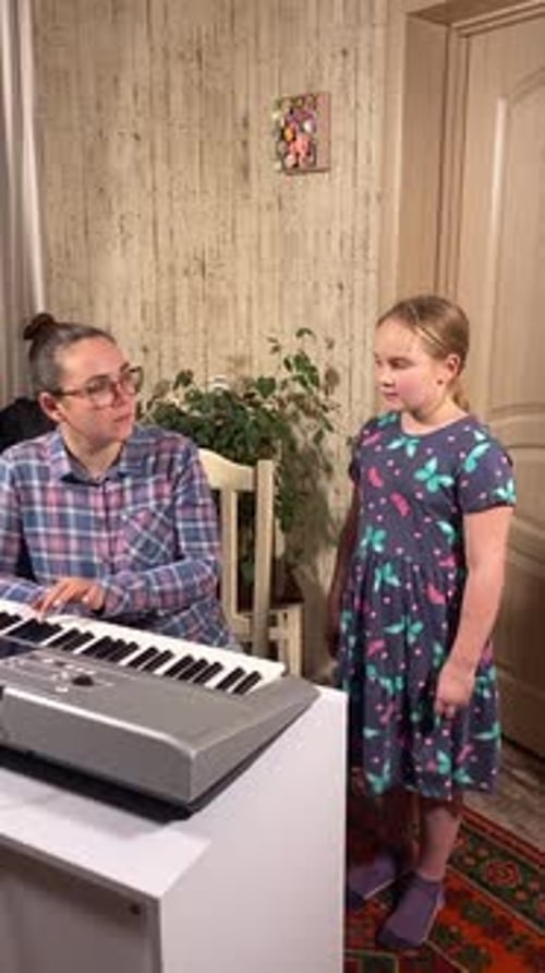 Woman Plays Piano as Young Girl Sings at Home