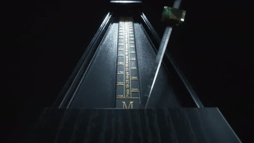 Dolly shot of an old-fashioned black metronome swinging back and forth