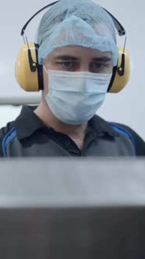 Male Worker In Mask Hairnet And Headphones During Operation In A Beer Factory Medium Shot