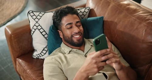 Man Relaxing on Couch Uses Mobile Phone