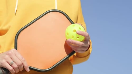 Person Holding Pickleball and Paddle Under Blue Sky