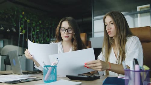 Two Women Collaborating in an Office Setting Reviewing Documents and Discussing Ideas During a