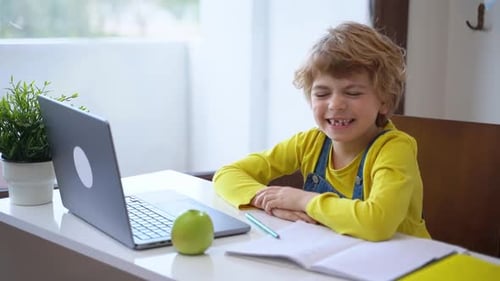 Cute Child Waves in Front of Laptop at Table