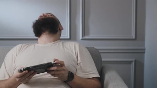 Man Plays Handheld Console Relaxing on Couch