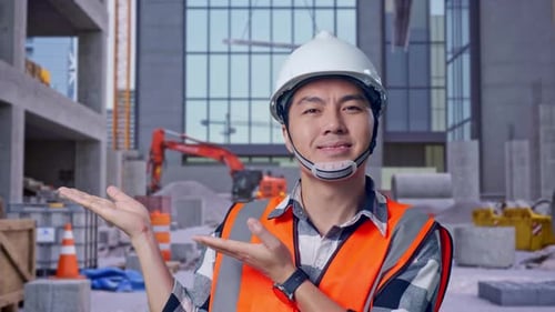 Close Up Of Asian Male Engineer Smiling And Pointing To Side at Construction Site