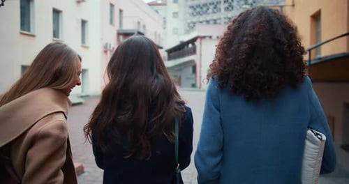 Camera Follows Three Happy Young Diverse Female Friends in Coats Walking Along Old City Street