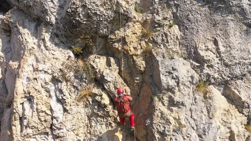 Flying near a mountain rescuer rappelling on a rocky wall with a drone