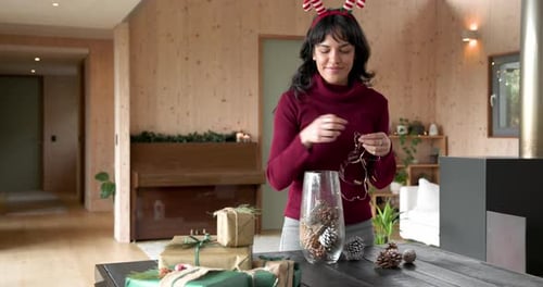 Woman decorating with fairy lights at home, preparing for Christmas celebration