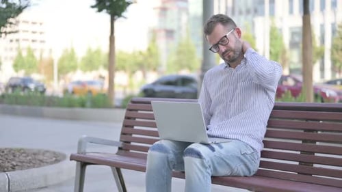 Man Uses Laptop, Rubs Neck on Park Bench