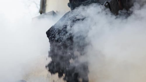 Heavy paver machinery dropping fresh hot black asphalt bitumen on the ground with smoke