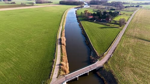High-angle shot of a rural landscape featuring a bridge crossing a straight river The scene includes