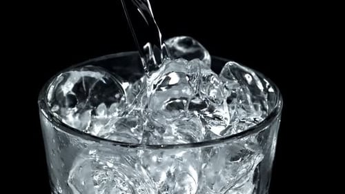 Water Pouring Into a Glass of Ice Cubes