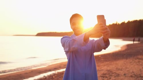 Happy Woman Takes Selfie at Beach During Sunset