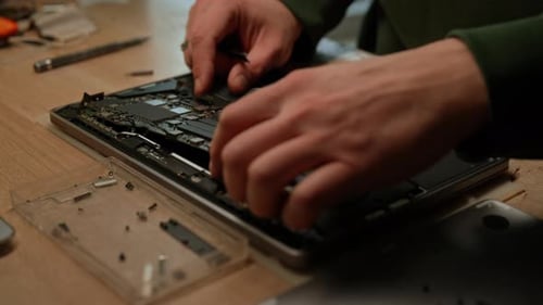Nahaufnahme eines Elektronikers, der das Motherboard vorsichtig in der Hand hält, während er den Laptop in der Werkstatt repariert