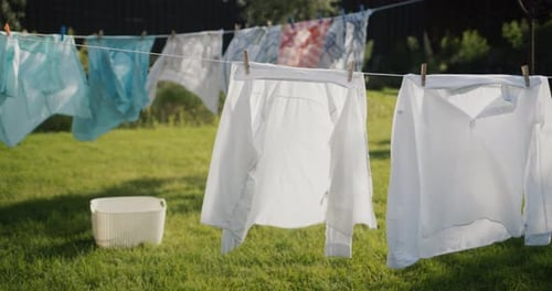 Roupas e roupas de cama estão secando no quintal da casa, um cesto de roupa suja está parado no