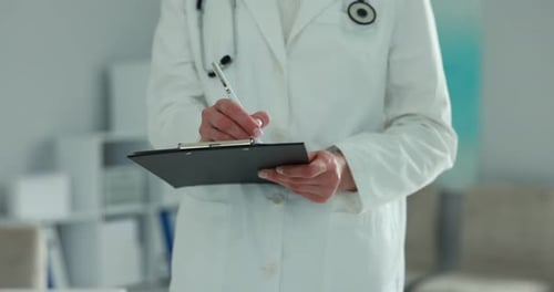 Doctor with stethoscope writing in clipboard indoors, closeup. Camera moving left