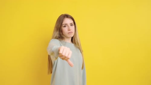 Woman Gives Thumbs Down on Yellow Background