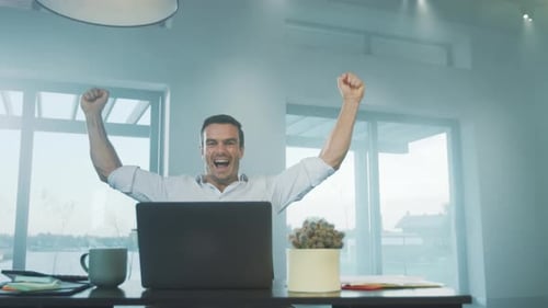 Excited man celebrating success at desk on laptop