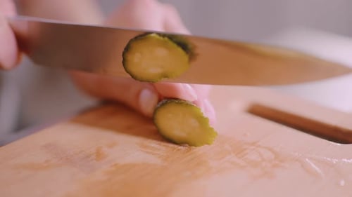 Close Up Hand Slicing Cucumber with Knife on Wooden Cutting Board