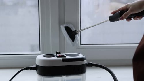 Frau putzt Fensterrahmen zu Hause mit Dampfreiniger, Nahaufnahme. Kamera bewegt sich nach unten, vorne und oben