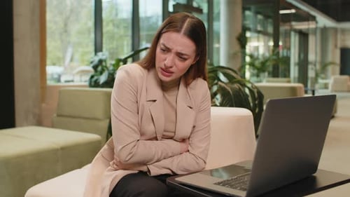 Disappointed Caucasian Businesswoman Using Laptop and Feeling Sudden Stomach Ache in Office Lobby