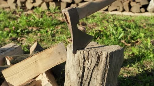 Axe stuck in wood log with a pile of chopped firewood, slider