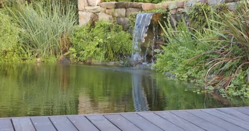 Camera panning over wooden deck as stone spillway feeding pond and making ripples for circulation