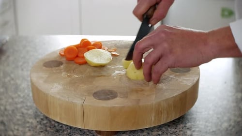 Un chef coupe une pomme de terre en quartiers pour en faire des chips et des frites dans une cuisine sur une planche à découper avec un