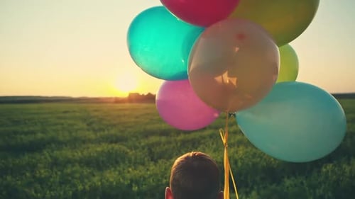 Young Boy Holding Balloons in a Field at Sunset
