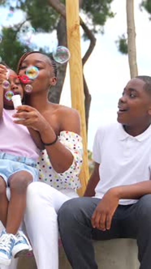 African black ethnic family with children in playground having fun blowing soap bubbles