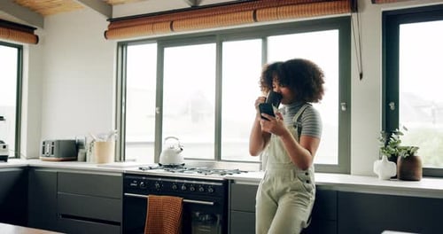 Woman Drinks Coffee, Uses Phone in Modern Kitchen