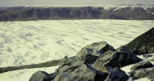 Vast Icy Landscape with Rocky Foreground and Distant Mountains in Winter