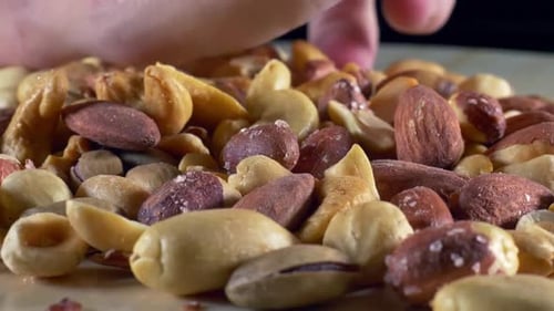 Hand Reaches Into a Pile of Mixed Salted Nuts