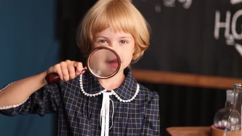 Smiling Child Looks Through Magnifying Glass in School