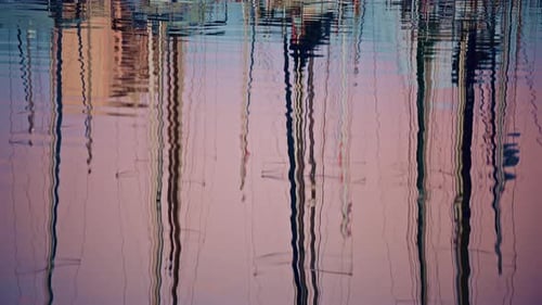 Close up of rippling water reflecting sailboat masts and harbor structures, forming abstract vertica