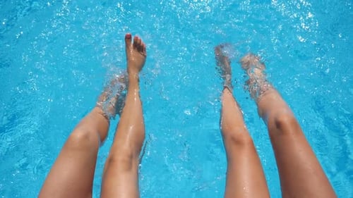 Top View on Female Legs Splashing Crystal Clear Water in Pool of Hotel