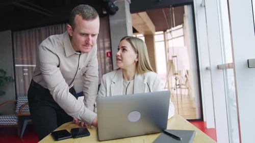 Male colleague bent over the woman sitting at the desk. Man pressing keys on computer.