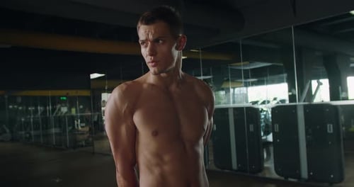 Junger Bodybuilder-Mann mit muskulösem Körper steht im Fitnessstudio