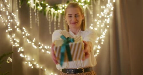 Woman Presents Gift with Ribbon and Holiday Lights